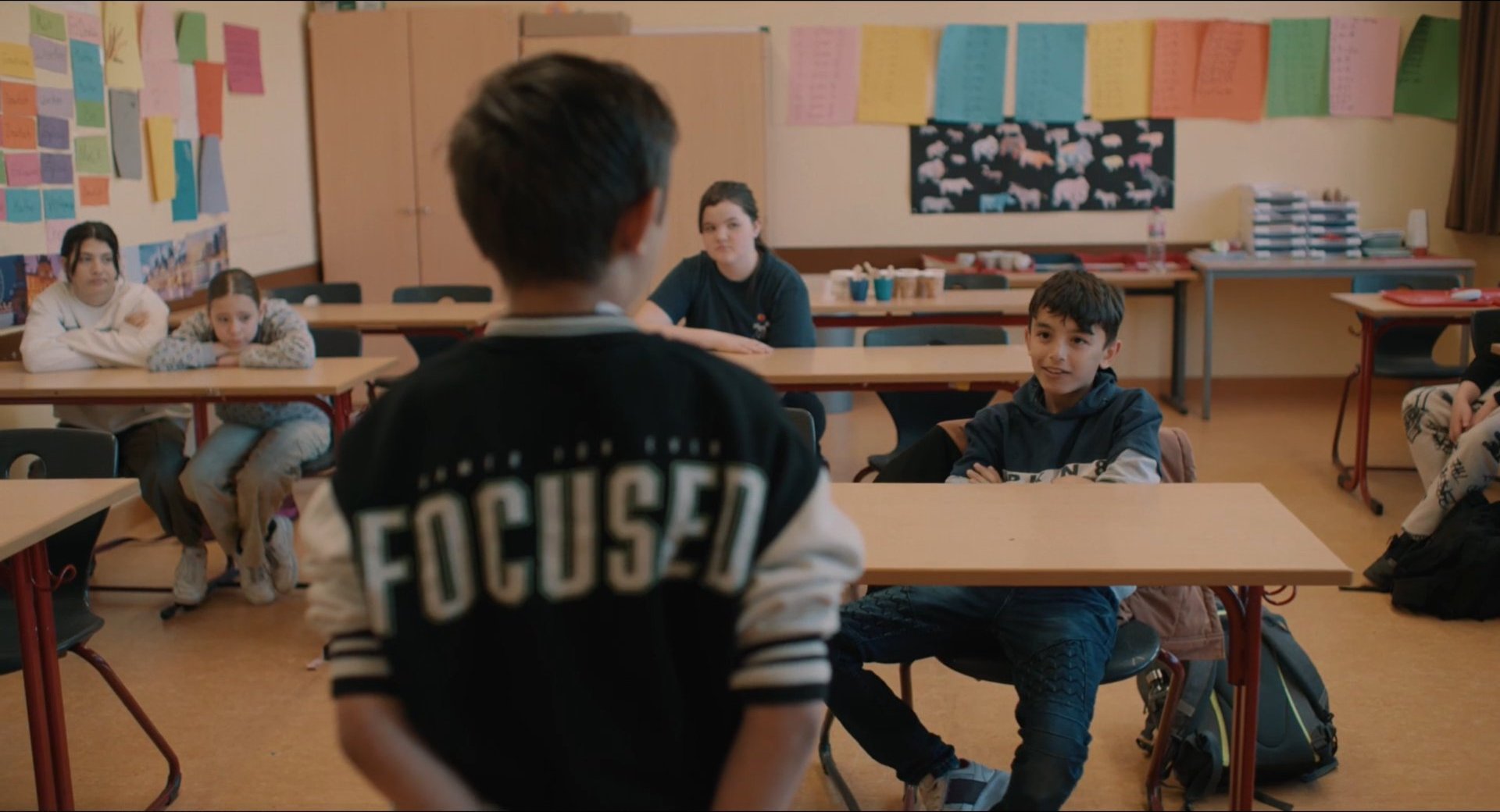 Filmbild aus dem Film ZIRKUSKIND zeigt Santino mit dem Rücken zur Kamera vor einer Schulklasse stehend