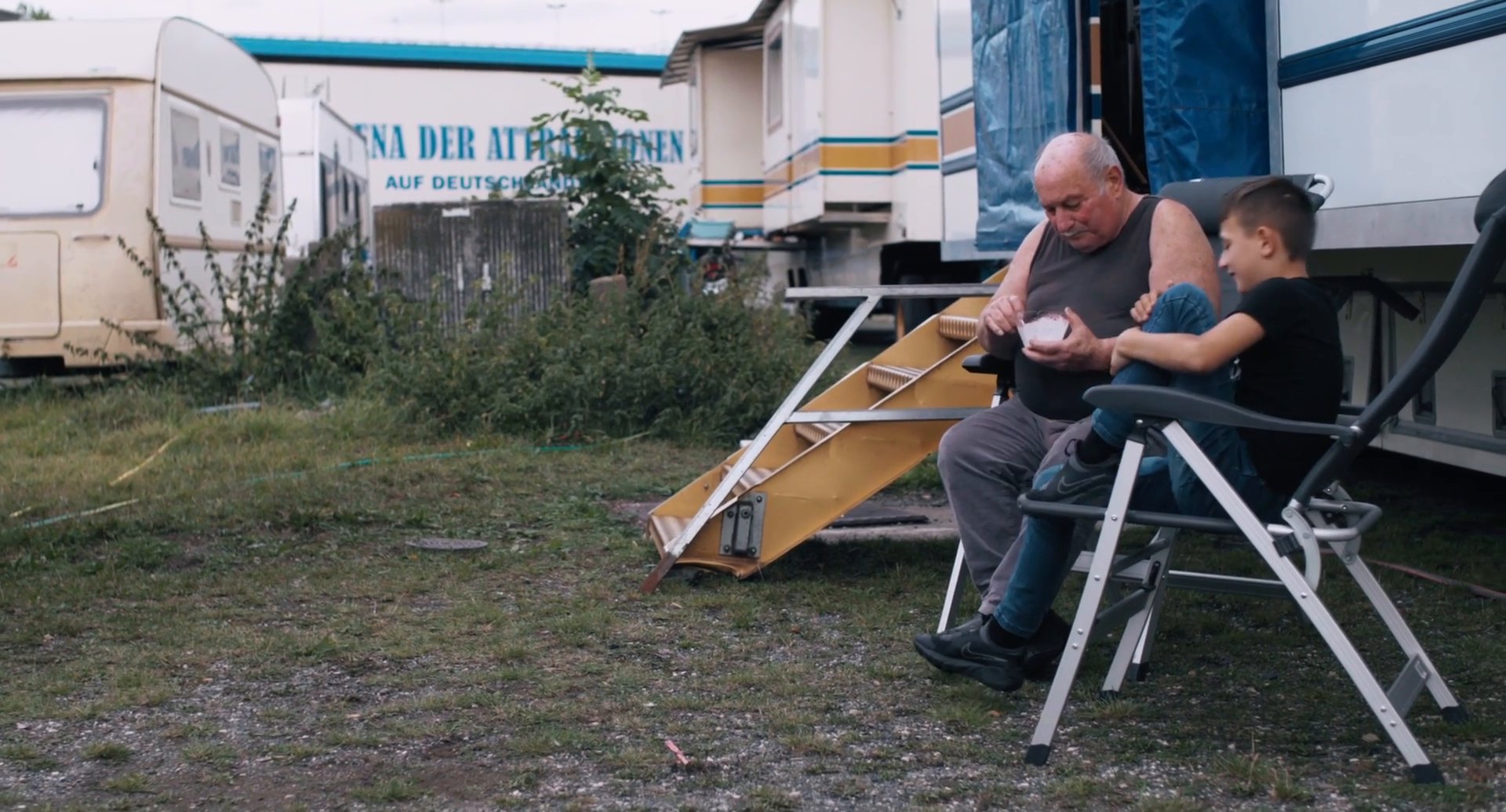 Filmbild aus dem Film ZIRKUSKIND zeigt Santino mit Uropa Ehe vor einem Zirkuswagen sitzend