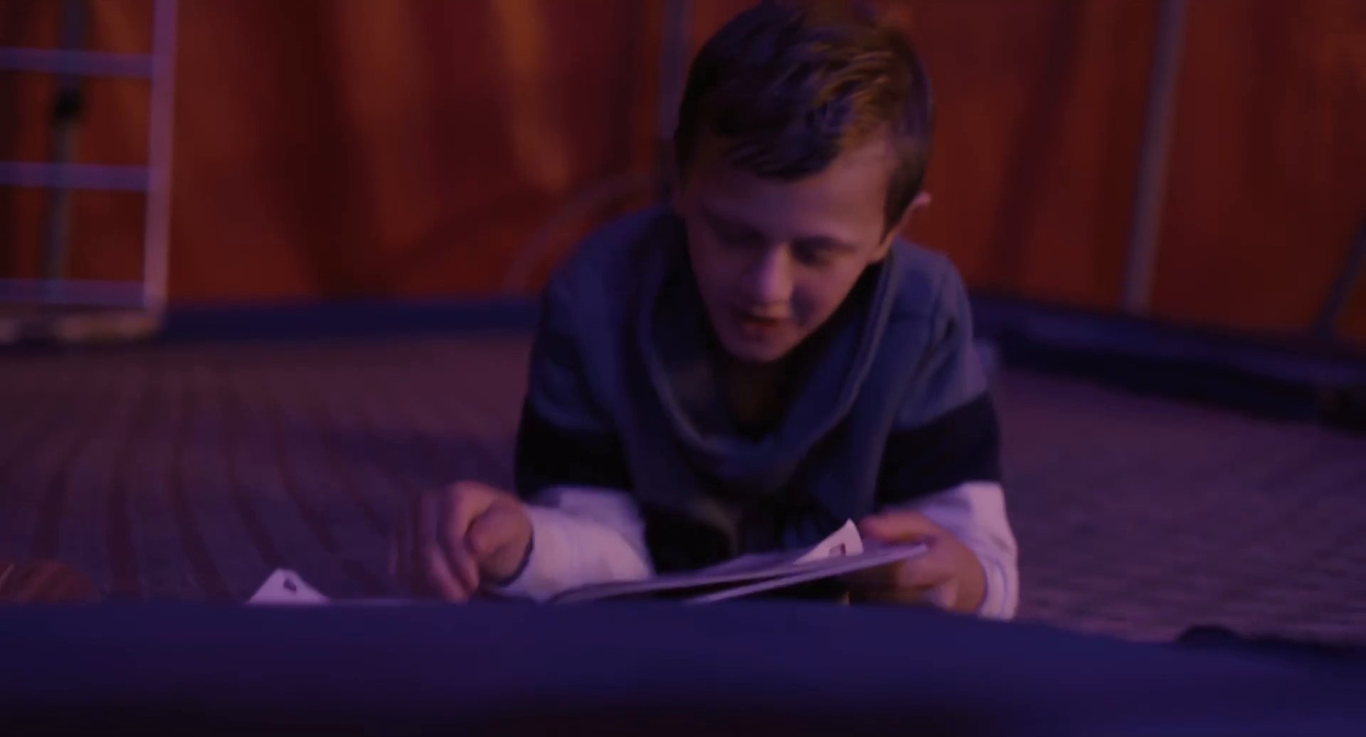 Filmbild aus dem Film ZIRKUSKIND zeigt Santino im Zirkuszelt auf einem Trampolin liegend in einem Buch lesen